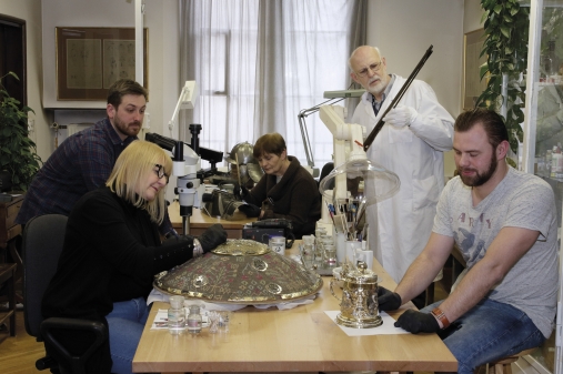 grupa osób w pracowni konserwacji rzemiosła artystycznego, na stołach obiekty zabytkowe